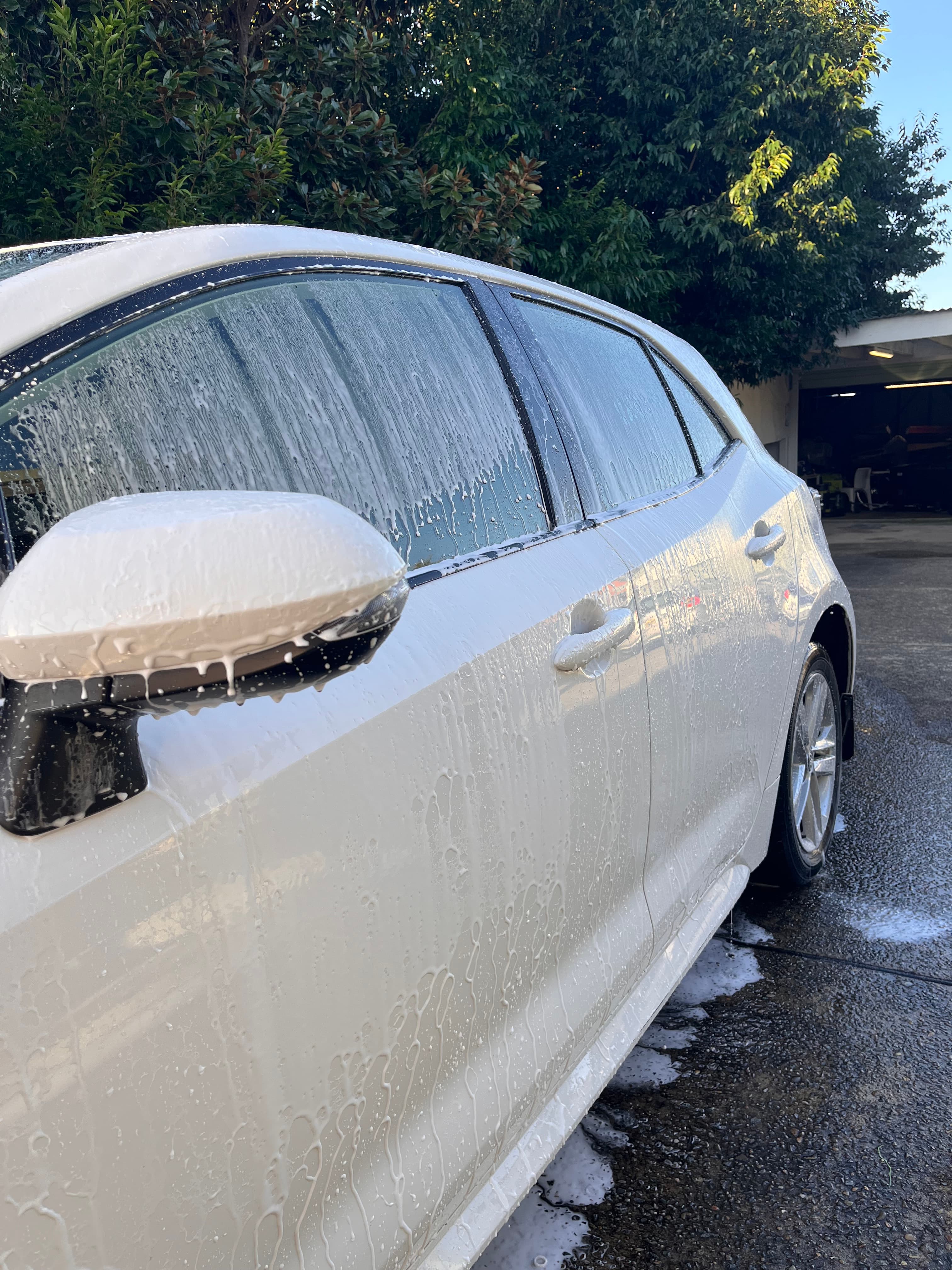 Thick white soap suds dripping down the side of a white car being washed.