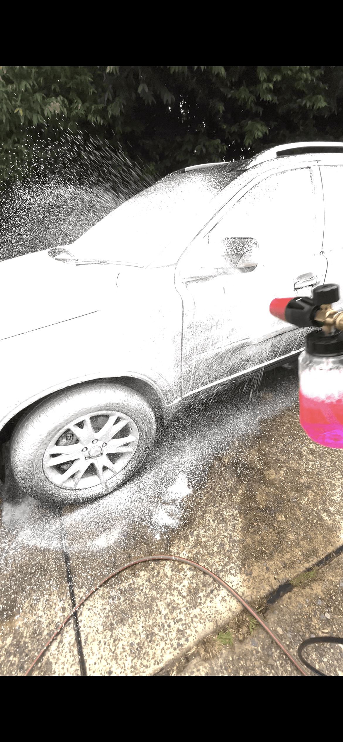 Thick white soap foam being sprayed onto a white SUV from a handheld foam cannon.